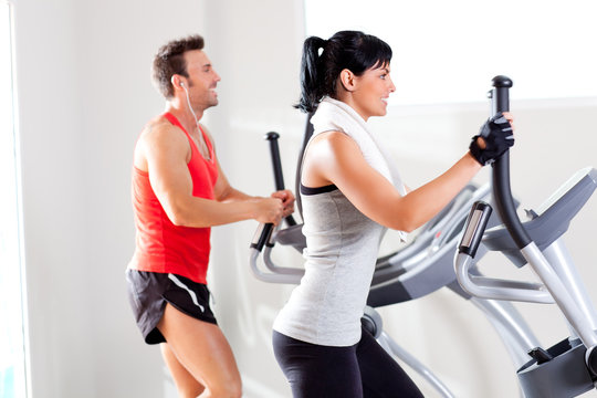 man and woman with elliptical cross trainer at gym