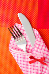 Fork and knife in a plaid cloth with a bow on a red tablecloth