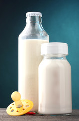 bottles of milk and soother on wooden table on blue background