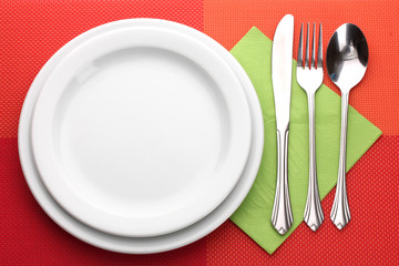 White empty plate with fork, spoon and knife on a red tablecloth