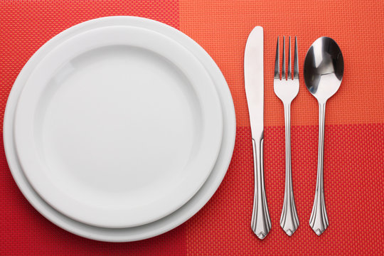 White empty plate with fork, spoon and knife on a red tablecloth