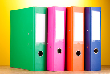 bright office folders on wooden table on yellow background.