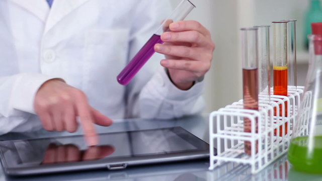 scientist working on tablet computer and checking test tubes