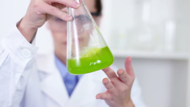 Female scientist mixing erlenmeyer flask with green chemicals