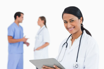 Fototapeta premium Smiling doctor with clipboard and colleagues behind her