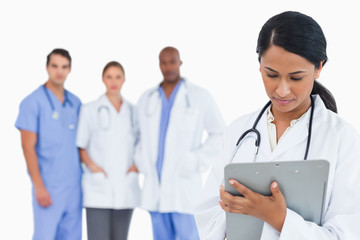 Female doctor taking notes on clipboard with staff members behin