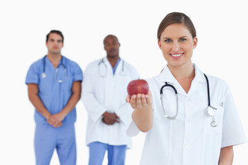 Fototapeta premium Doctor offering apple with colleagues behind her