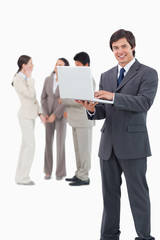 Smiling salesman with laptop and team behind him