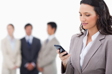 Saleswoman writing text message with colleagues behind her