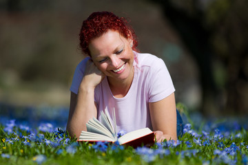 rothaarige frau liegt auf einer blumenwiese und liest ein buch