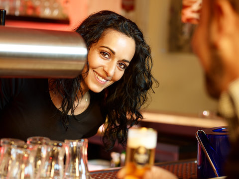 Mediterranean looking bar-maid enjoys her work at a pub