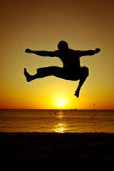 Silhouette of a man jumping on the beach at sunset