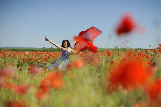 Girl dancing in poppies with flying red cloth
