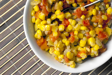 A salad of corn, peppers and tomatoes on a background of bamboo.