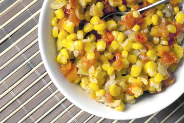 A salad of corn, peppers and tomatoes on a background of bamboo.