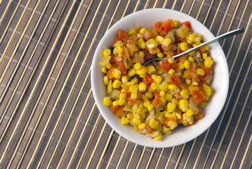 A salad of corn, peppers and tomatoes on a background of bamboo.