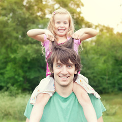 Obraz premium Young man holding blonde little girl on shoulders in park
