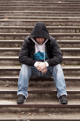 Sad teenage boy with hood sitting on stairs - 38263991