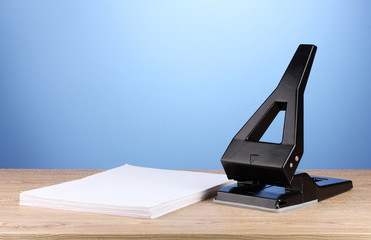 Black office hole punch with paper on blue background