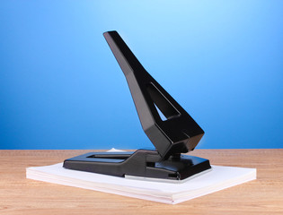 Black office hole punch with paper on blue background