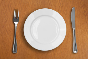 round white plate, knife and fork on wooden table