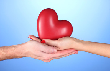Fototapeta na wymiar Man and woman holding red heart in hands on blue background
