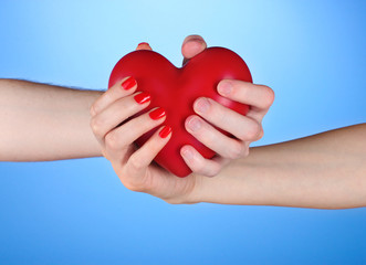 Obraz premium Man and woman holding red heart in hands on blue background