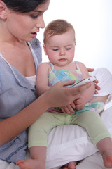 Mother resting baby on knee whilst looking at mobile telephone