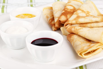 Several thin pancakes with butter, sour cream and jam