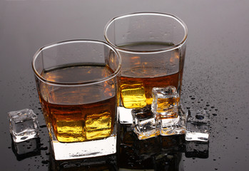 two glasses of scotch whiskey and ice on grey table