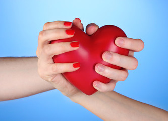 Man and woman holding red heart in hands on blue background