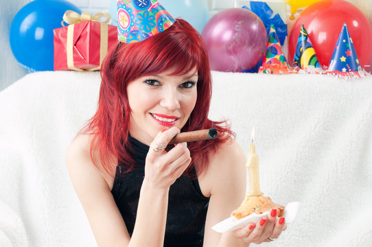 Smiling party girl lighting a cigar from a birthday cake