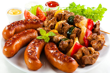 Grilled meat, sausages and vegetables on white background