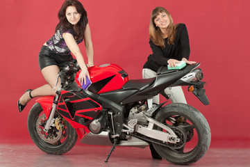 Fototapeta na wymiar Two young girls wash a bike, on red background