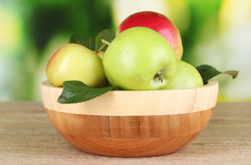Fresh organic apples in plate on wooden table outside