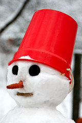 A snowman with a red pail on his head.