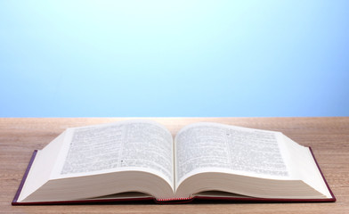 Open book on wooden table on blue background