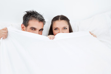 Mann und Frau verstecken sich hinter Bettdecke