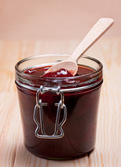 Strawberry jam in glass jar with wooden spoon.