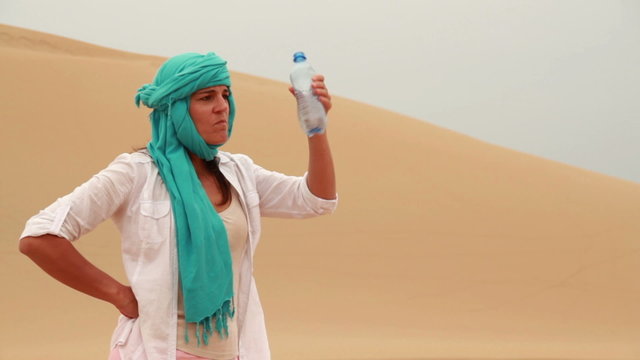 Thirsty woman drinkig water from bootle in the desert