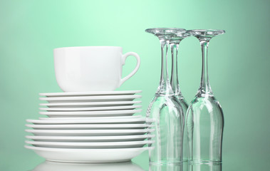Clean plates, cup and glasses on green background