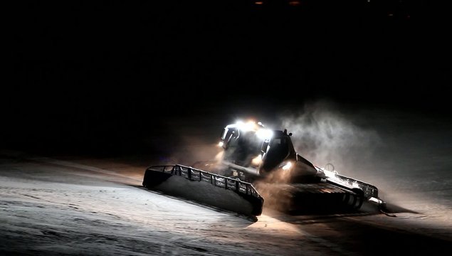 Snowcat grooming a ski slope during the night.  Front view of the snow plough with headlights