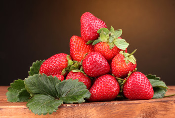 Strawberries with leaves on wooden table on brown  background