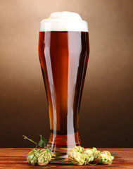 beer in glass and green hop on wooden table on brown background