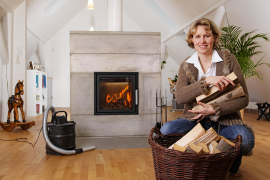 blond lady with firewood in front of a fireplace