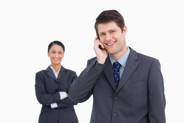 Close up of smiling salesman on the phone with colleague behind