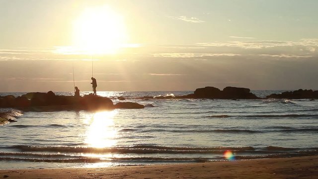 A man and a woman fishing in the sea at sunset