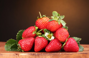Strawberries with leaves on wooden table on brown  background
