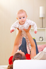 Baby playing with mother on divan