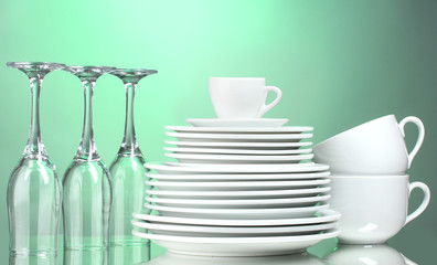 Clean plates, cups and glasses on green background